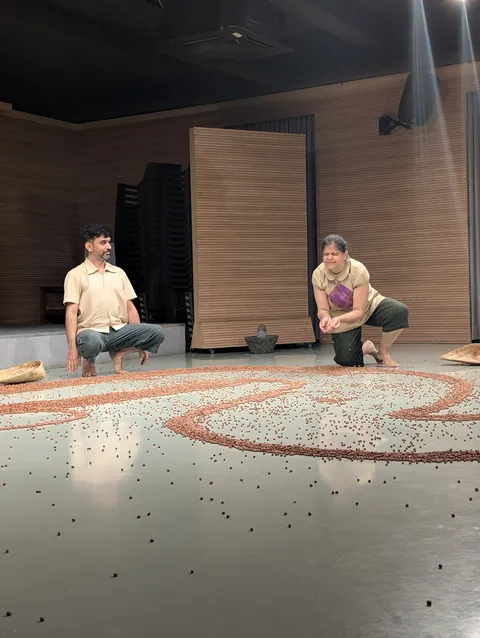 Two performers crouch at either end of a long trail of black gram.