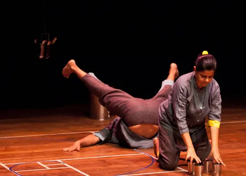 The two performers meet over a stack of steel plates.