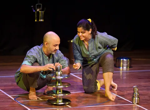 A performer balances a tower of steel bowls.