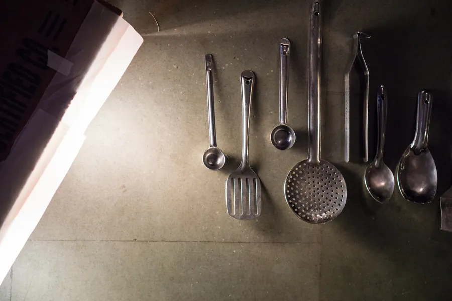 Steel ladles, a slotted spoon and serving spoons laid out on a concrete floor.