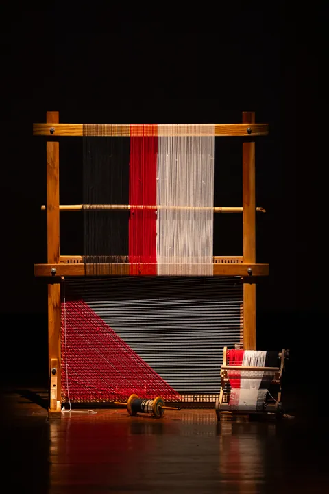 The loom alone on a dark stage, its weave complete in red, white and black.