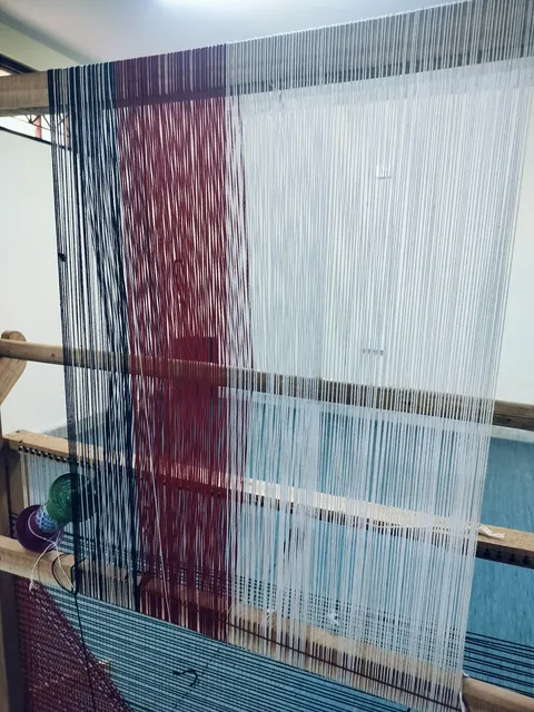 Close on the warp: fine threads in blue, red and white stretched taut.